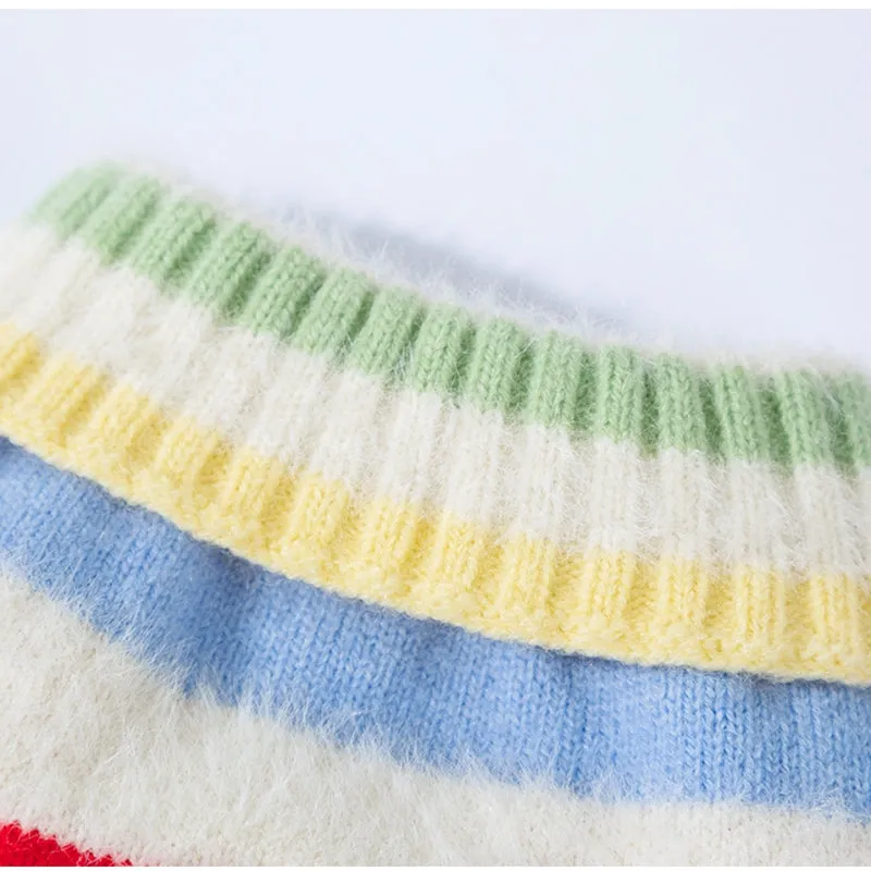 Corgi dog wearing a rainbow apple striped knitted pullover sweater in brown, standing on grass