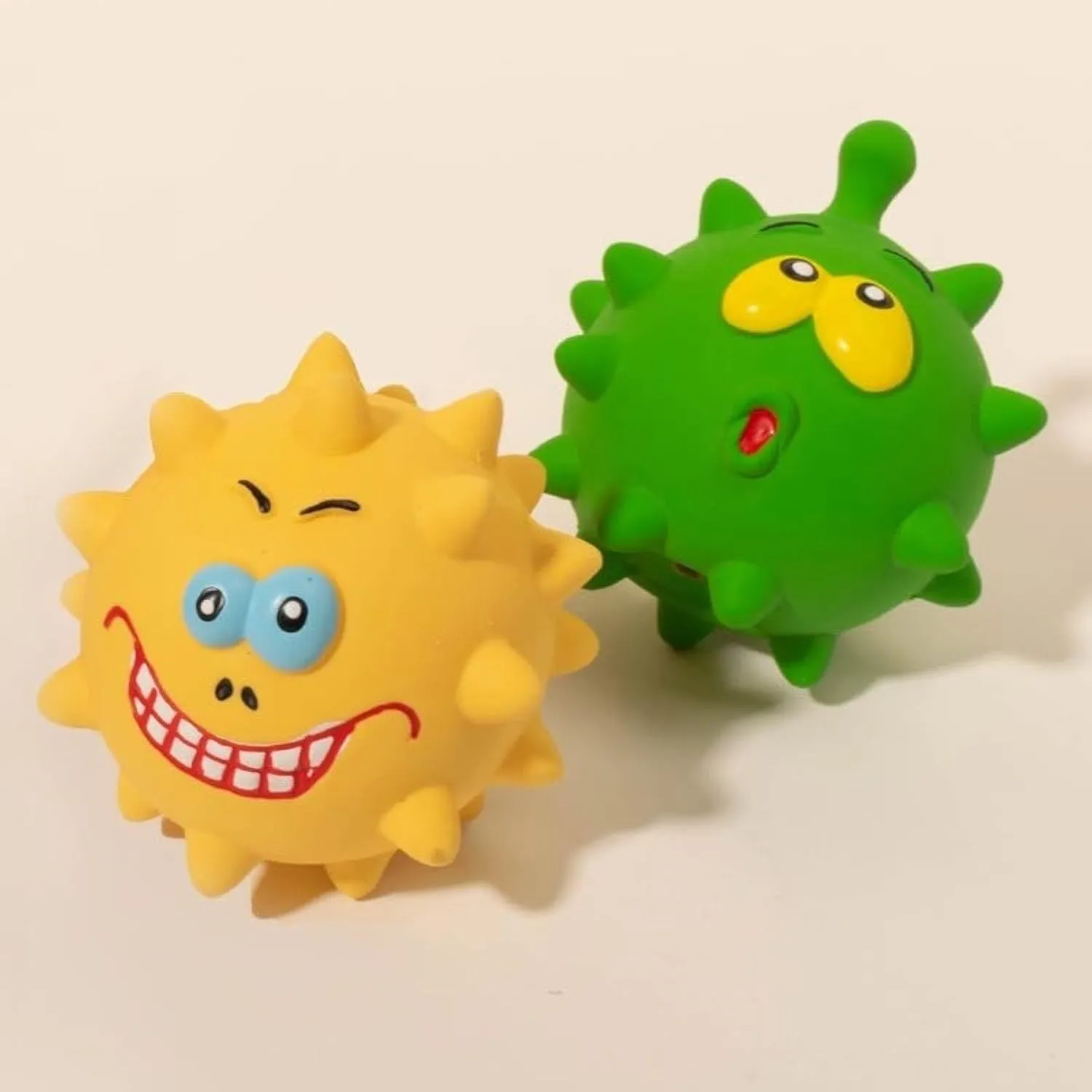 Set of four colourful latex squeaky dog balls with cute faces on a textured surface.