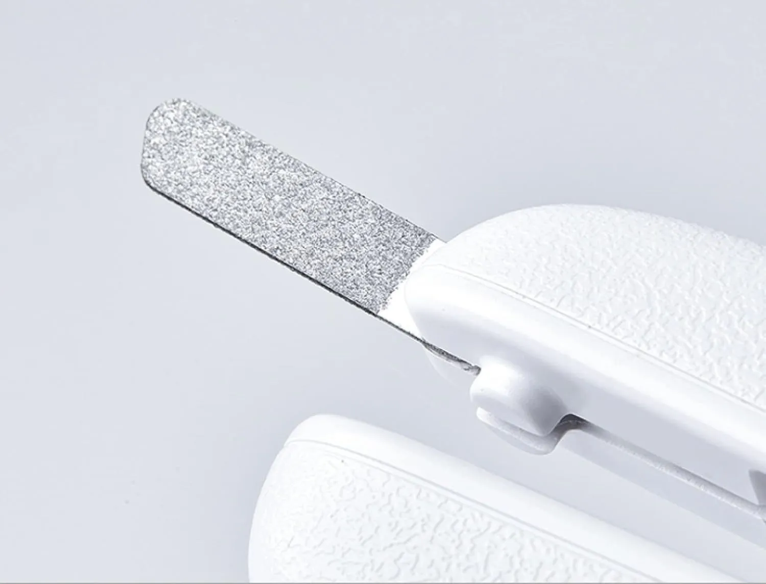 White pet nail clippers with LED light and transparent anti-splash guard next to a nail file on a table