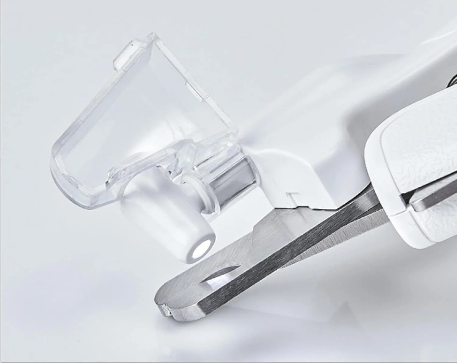 White pet nail clippers with LED light and transparent anti-splash guard next to a nail file on a table
