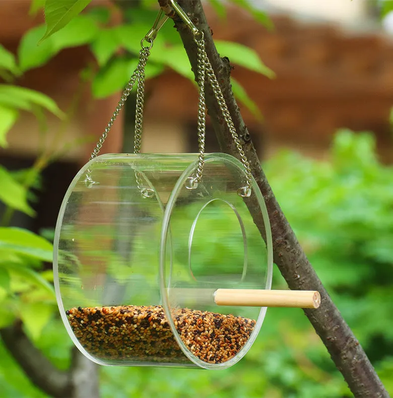 Round transparent acrylic bird food box with 1000ml seed capacity and visible seed inside, on a garden background