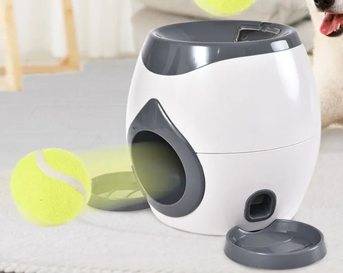Smart pet feeder reward machine with two tennis balls and treat dispenser in green and white colour, shown on a wooden floor