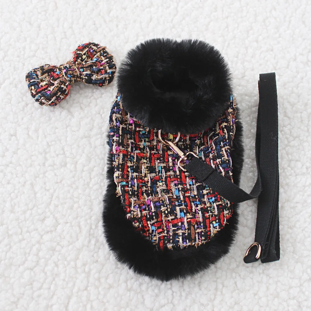 A dog wearing a classic cloth cloak attached to a chest strap with a hand holding rope