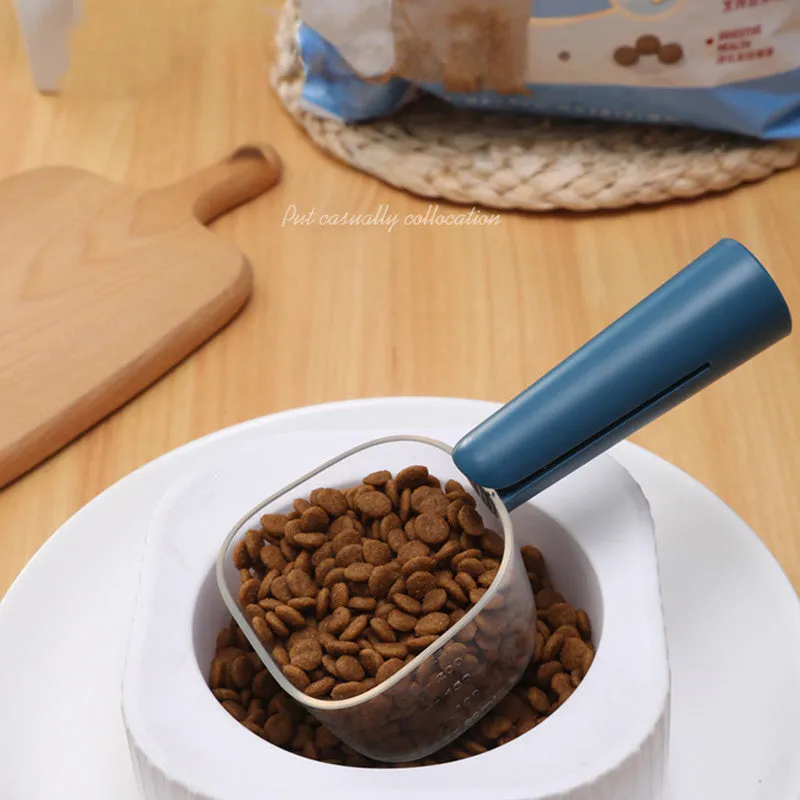 Transparent plastic pet food spoon with scale markings for measuring cat and dog dry food, available in Blue Pink White