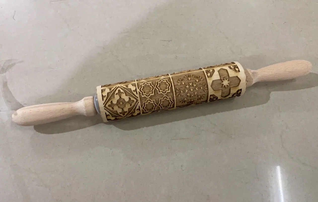 Wooden rolling pin with embossed Christmas patterns, 45cm long, on a kitchen worktop.