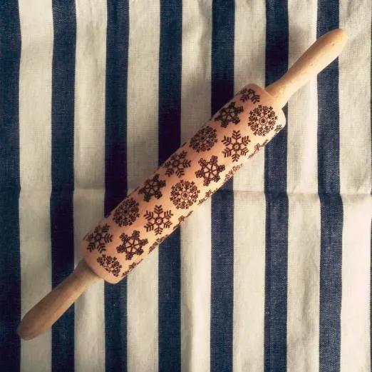 Wooden rolling pin with embossed Christmas patterns, 45cm long, on a kitchen worktop.