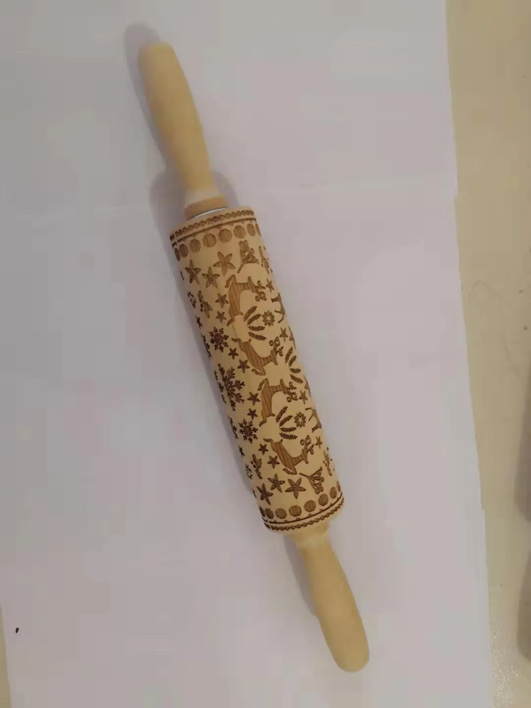 Wooden rolling pin with embossed Christmas patterns, 45cm long, on a kitchen worktop.