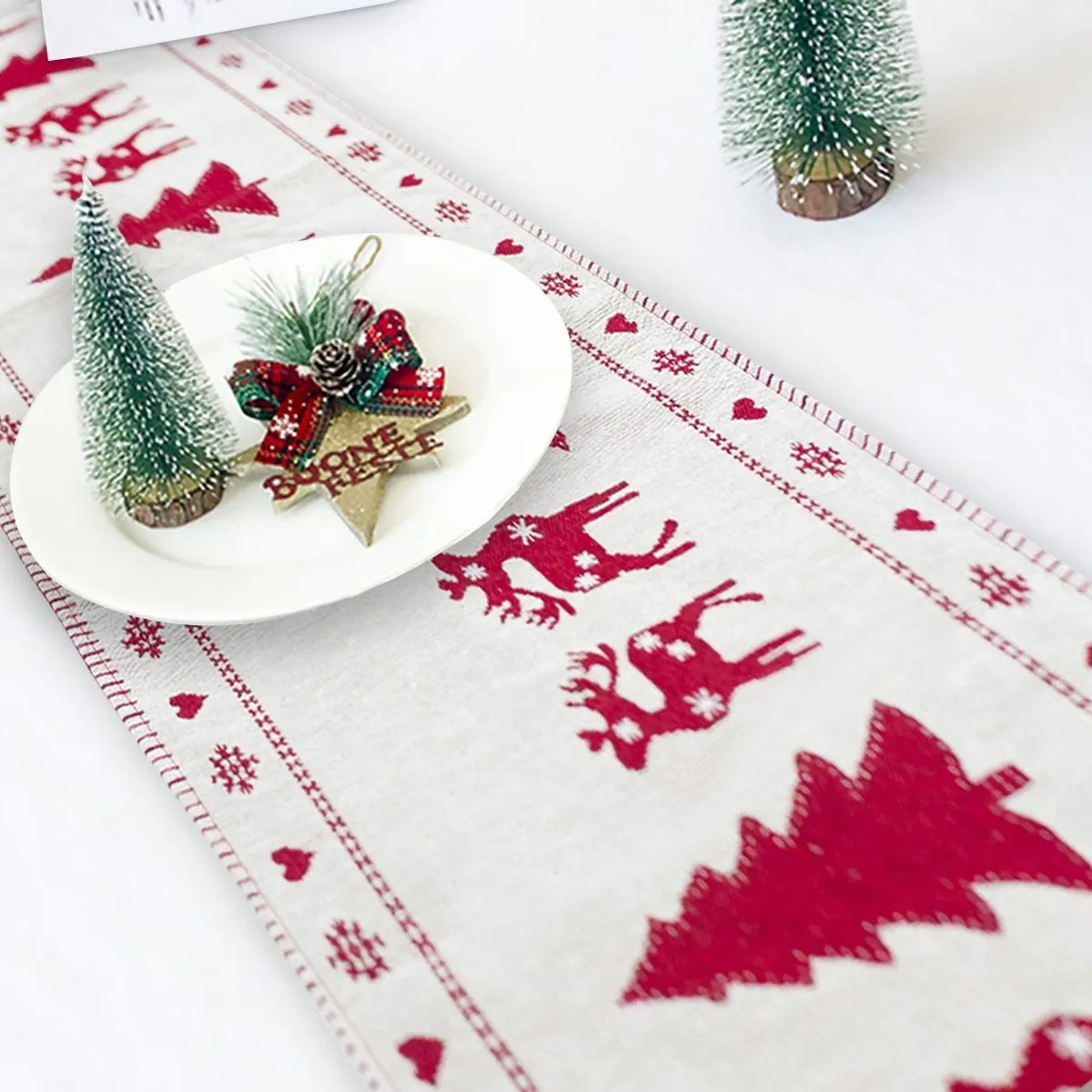 Red, white, and green Christmas table runner with elk and snowman print on a wooden dining table.