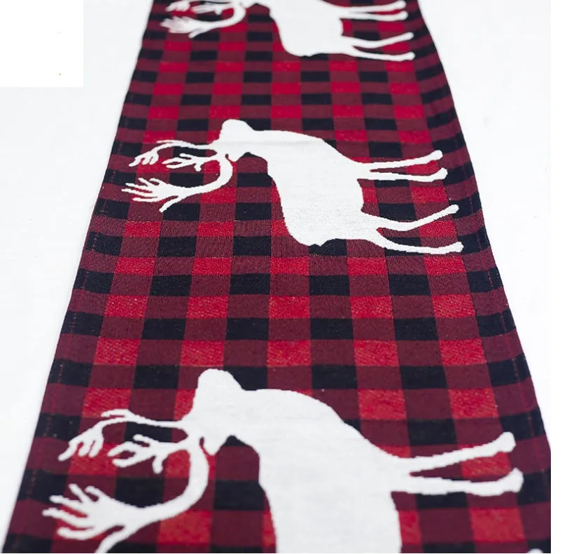 Red, white, and green Christmas table runner with elk and snowman print on a wooden dining table.