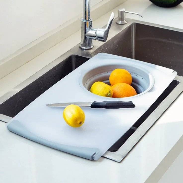 Grey 3-in-1 chopping board with detachable folding drain basket on a kitchen counter.