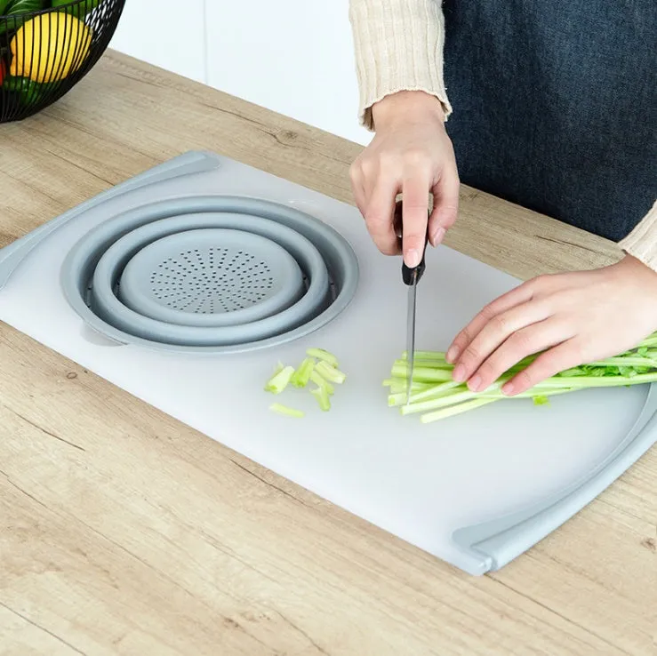 Grey 3-in-1 chopping board with detachable folding drain basket on a kitchen counter.