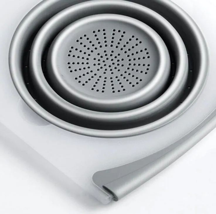 Grey 3-in-1 chopping board with detachable folding drain basket on a kitchen counter.