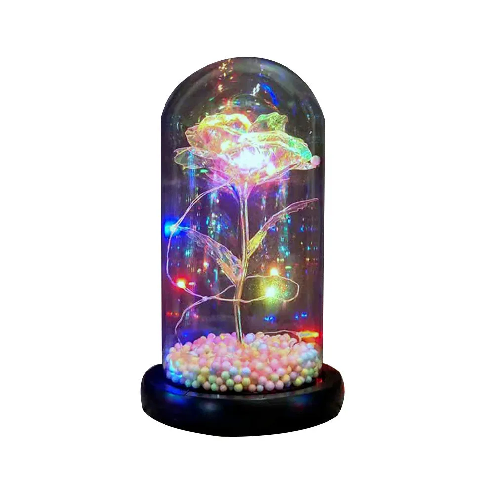Gold artificial roses inside a clear glass dome ornament with LED lights and decorative accessories.