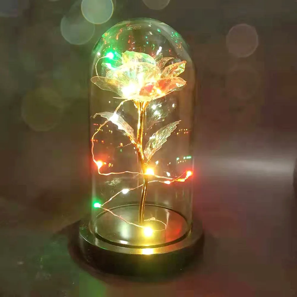 Gold artificial roses inside a clear glass dome ornament with LED lights and decorative accessories.