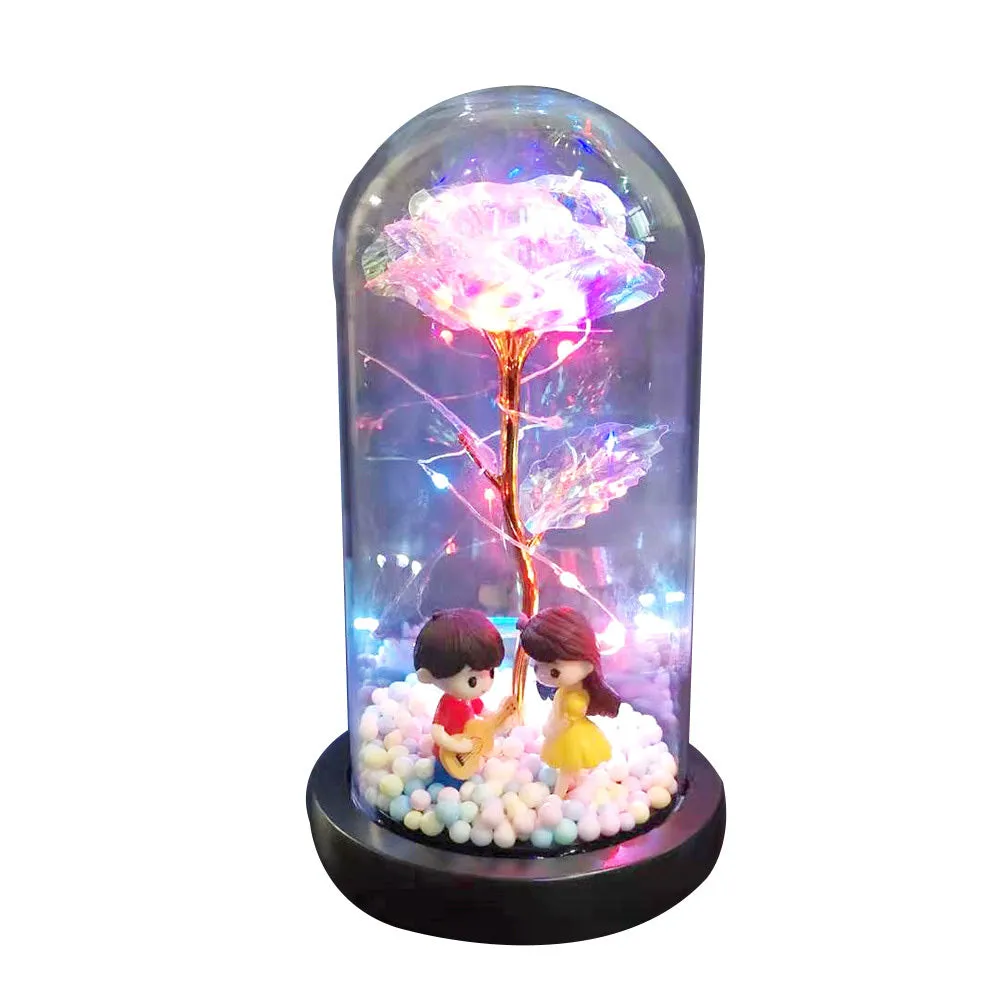 Gold artificial roses inside a clear glass dome ornament with LED lights and decorative accessories.