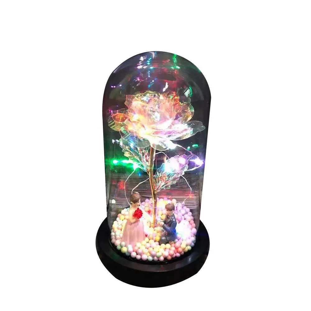 Gold artificial roses inside a clear glass dome ornament with LED lights and decorative accessories.