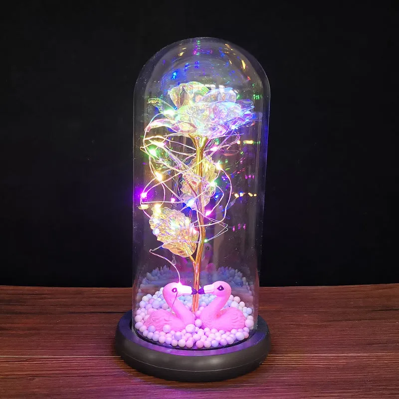 Gold artificial roses inside a clear glass dome ornament with LED lights and decorative accessories.