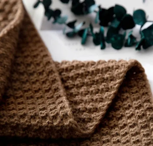 Simple modern fringed knit acrylic blanket in beige colour laid on a sofa, showing 130x170cm size.
