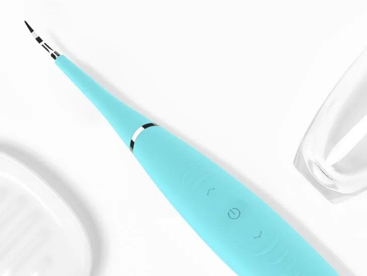 Pink or blue waterproof electric toothbrush care tool for removing dental calculus on a bathroom counter.