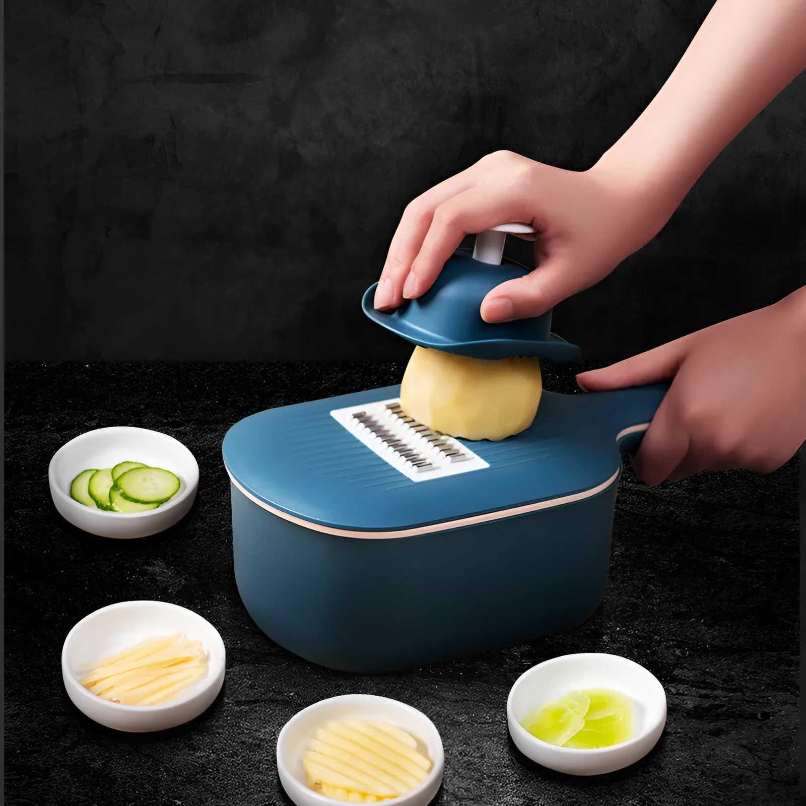 Dark blue vegetable cutter with four stainless steel blades, drain basket, and hand guard on a kitchen worktop