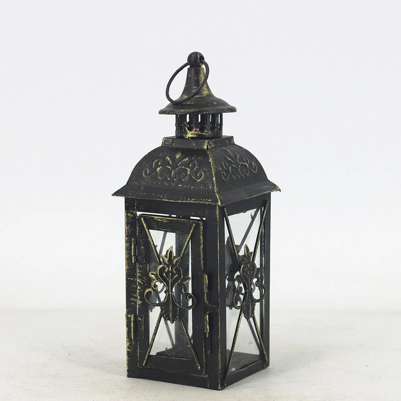 Black gold wrought iron floor standing storm lantern with tempered glass panels on a stone patio.