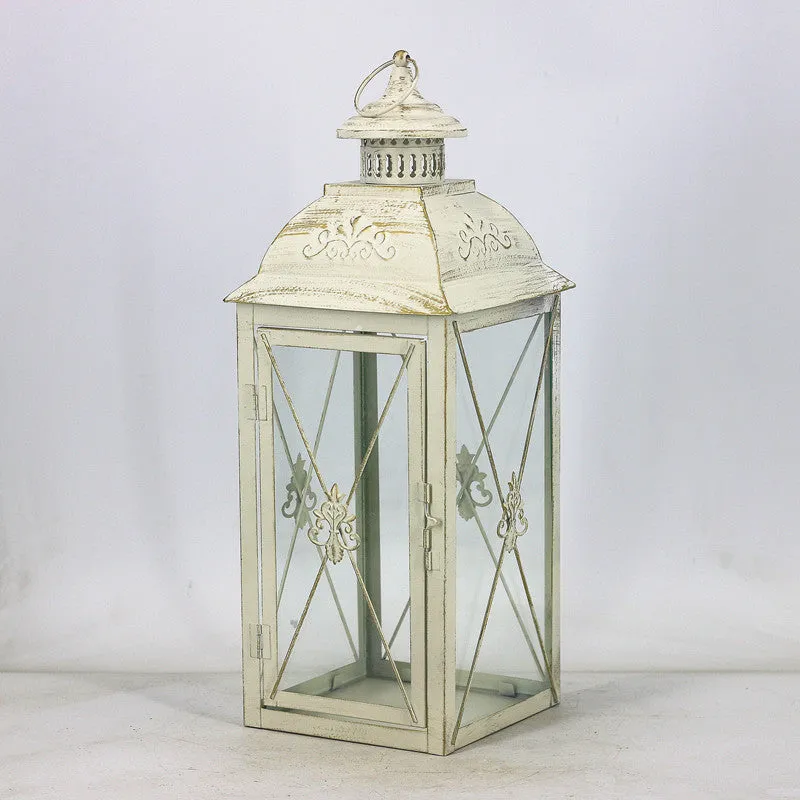 Black gold wrought iron floor standing storm lantern with tempered glass panels on a stone patio.