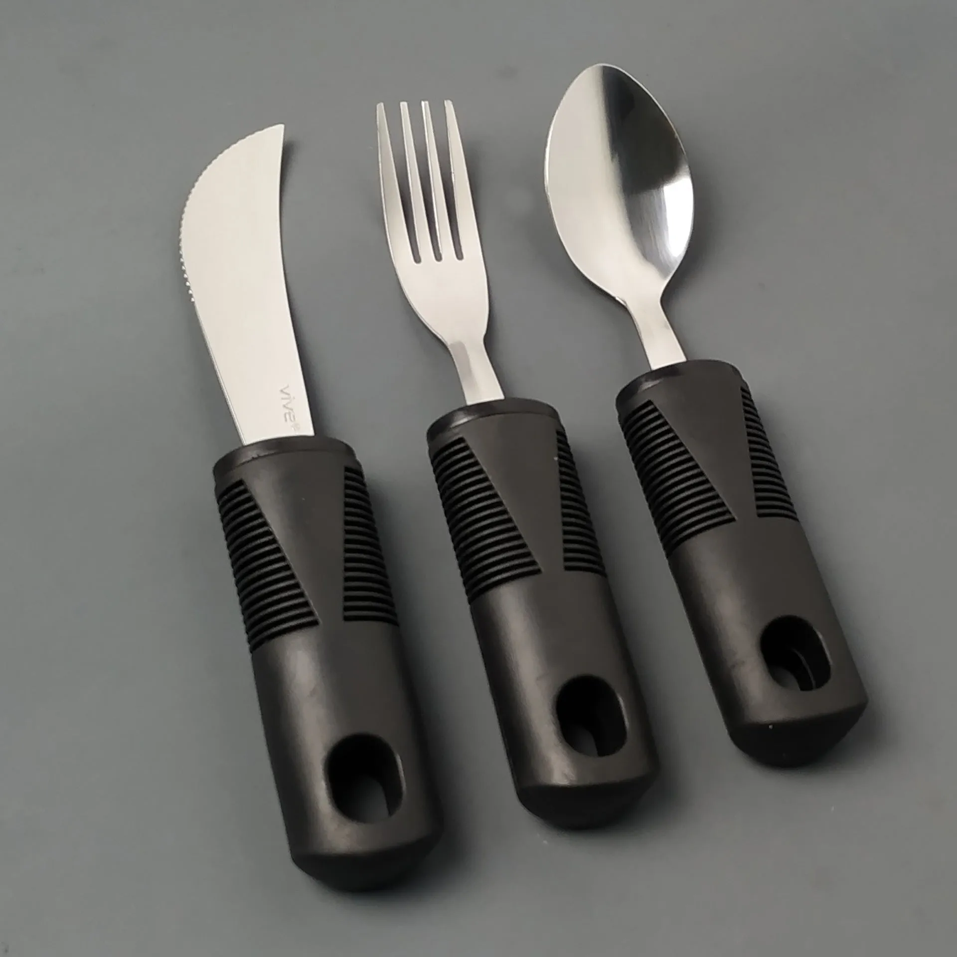 Stainless steel adaptive cutlery set with black rubber handles, showing knife, fork, and spoon.