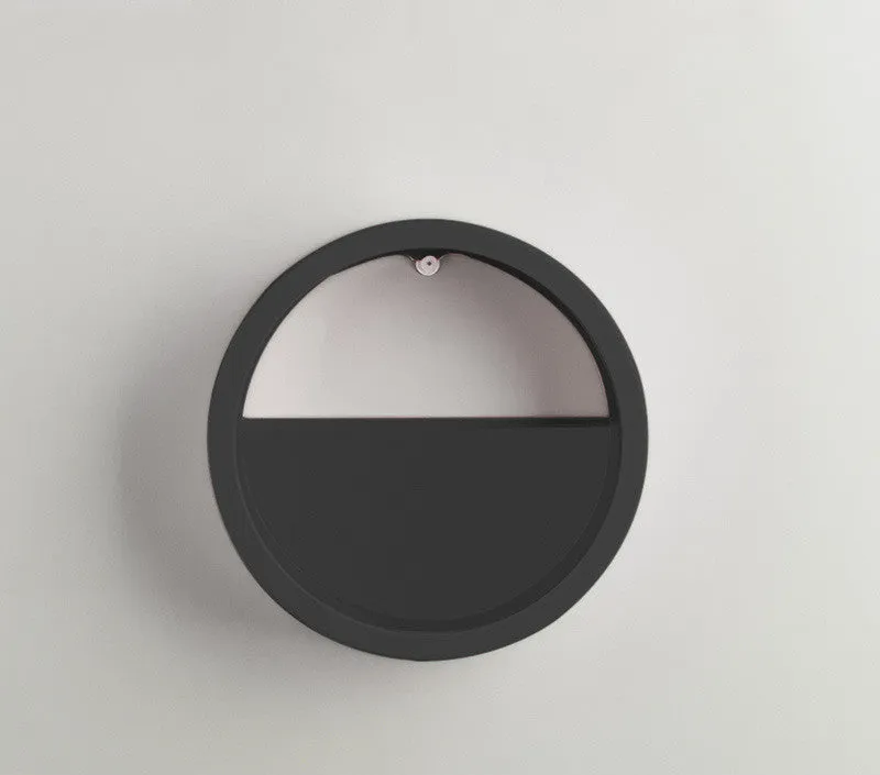 Round iron wall vase in black hanging on a wall with a succulent plant inside