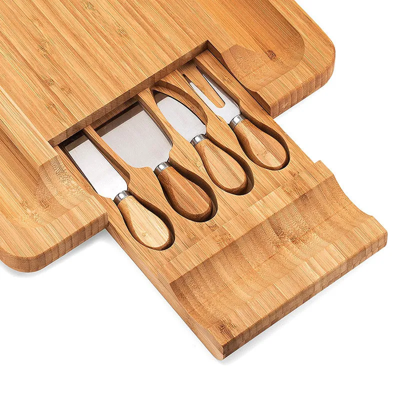 Square bamboo cutting board with drawer holding four-piece knife and fork set in wood colour