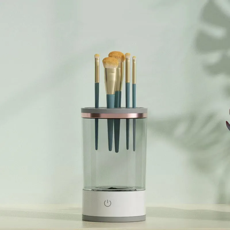 Grey and white electric makeup brush cleaner with USB charging cable on a wooden surface