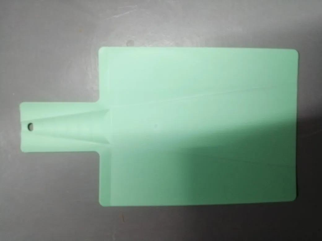 Green folding plastic cutting board with non-slip texture and hanging hole on kitchen countertop