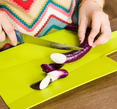 Green folding plastic cutting board with non-slip texture and hanging hole on kitchen countertop