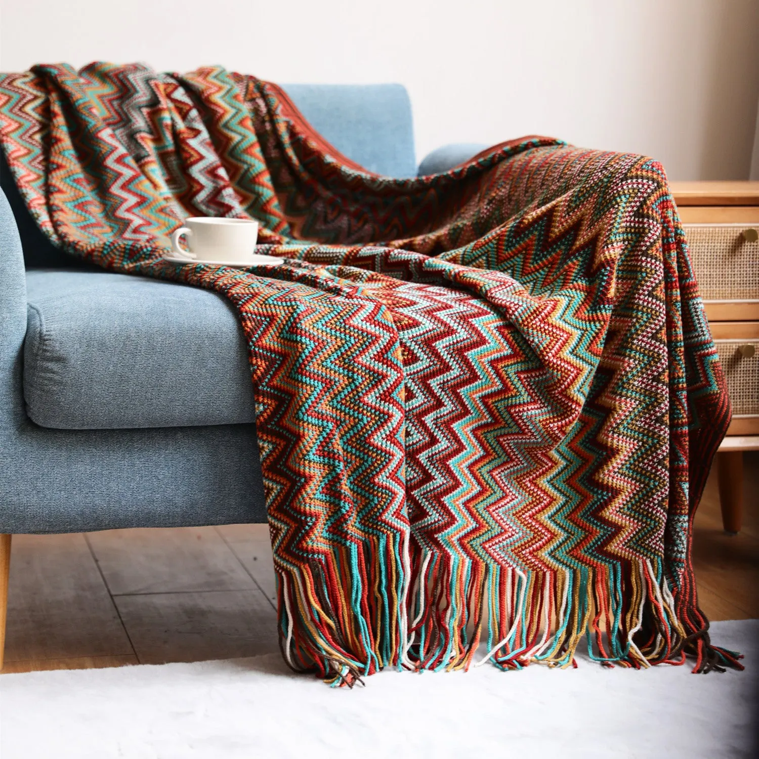 Blue knitted acrylic blanket with striped pattern and fringe, draped over a sofa