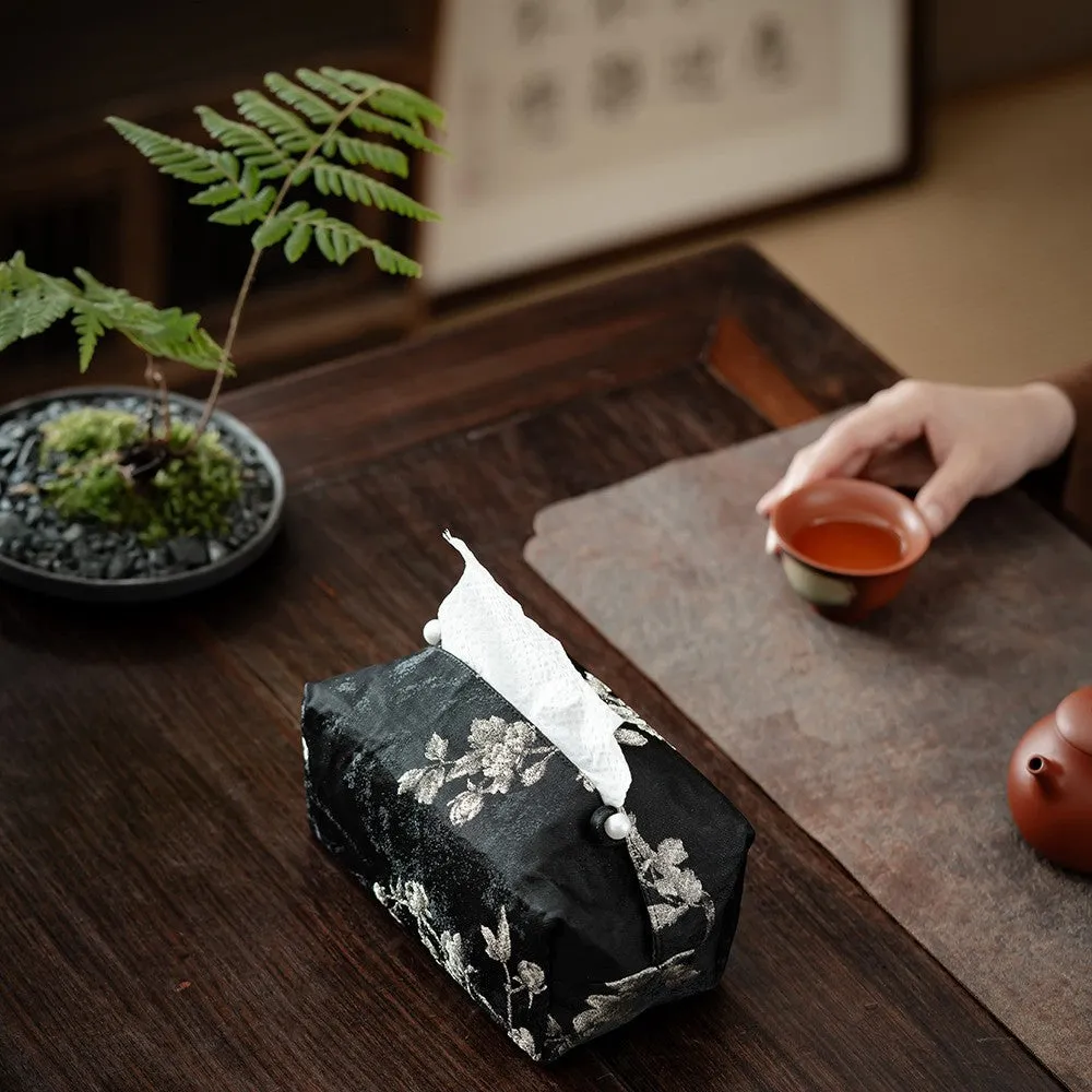 White Chinese brocade tissue box with embroidered plum blossoms on a side table.