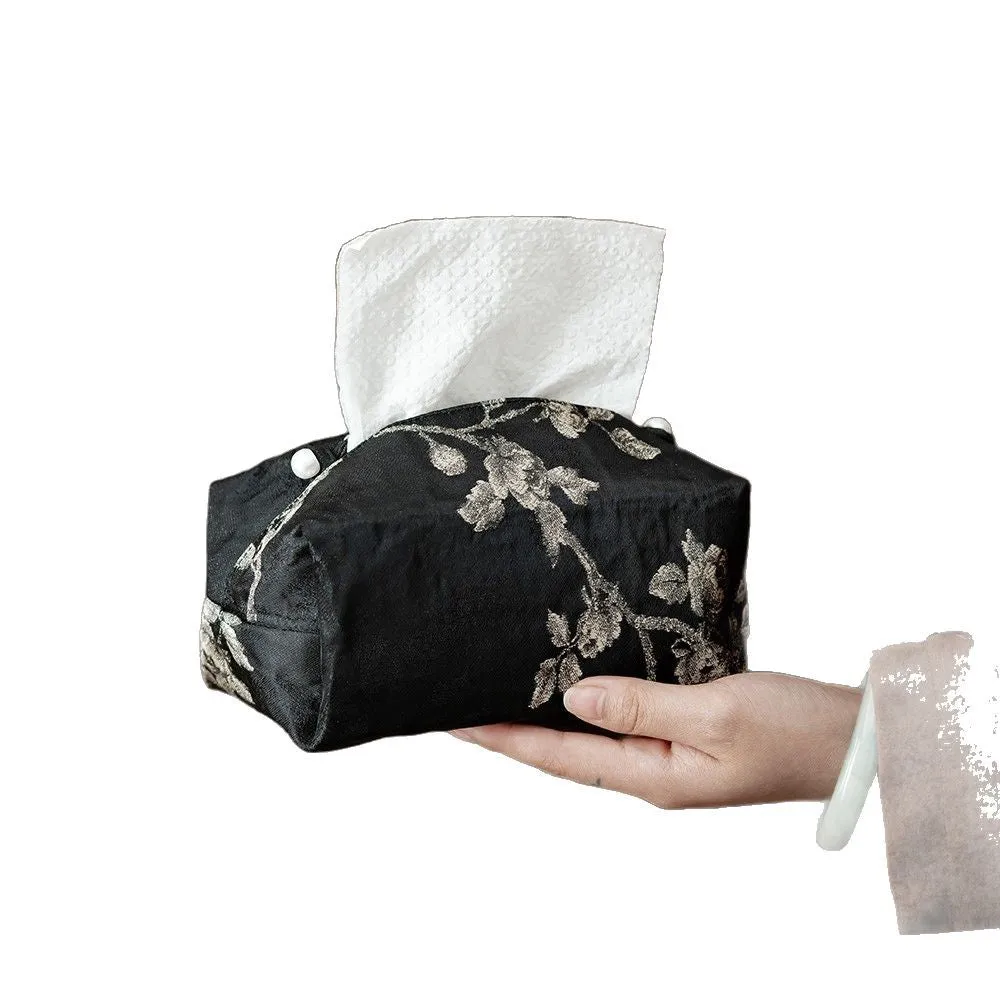 White Chinese brocade tissue box with embroidered plum blossoms on a side table.
