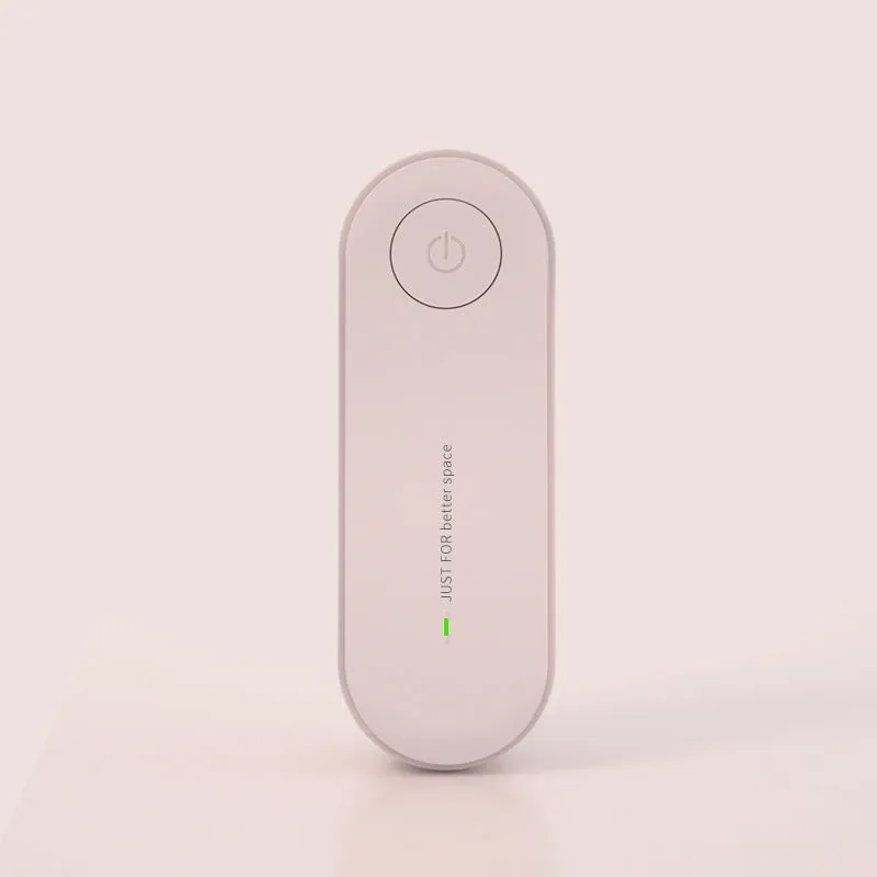 Small negative ion air purifier in black, plugged into a wall socket, with a room in the background