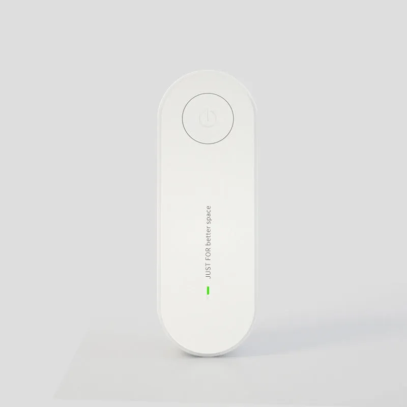 Small negative ion air purifier in black, plugged into a wall socket, with a room in the background