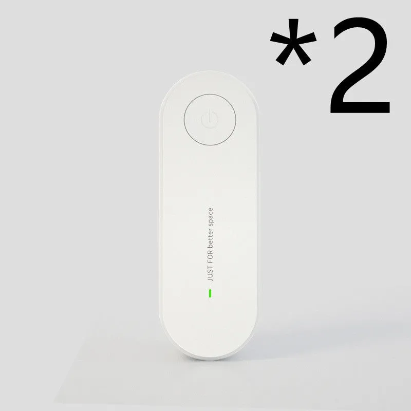 Small negative ion air purifier in black, plugged into a wall socket, with a room in the background