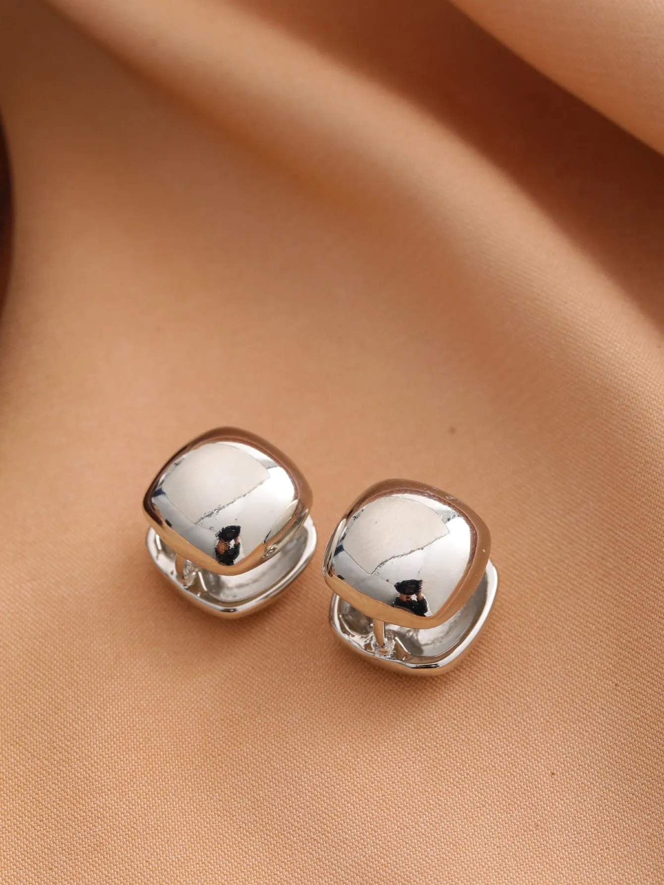 Smooth geometric hollow stud earrings in gold and silver colour options on a neutral background