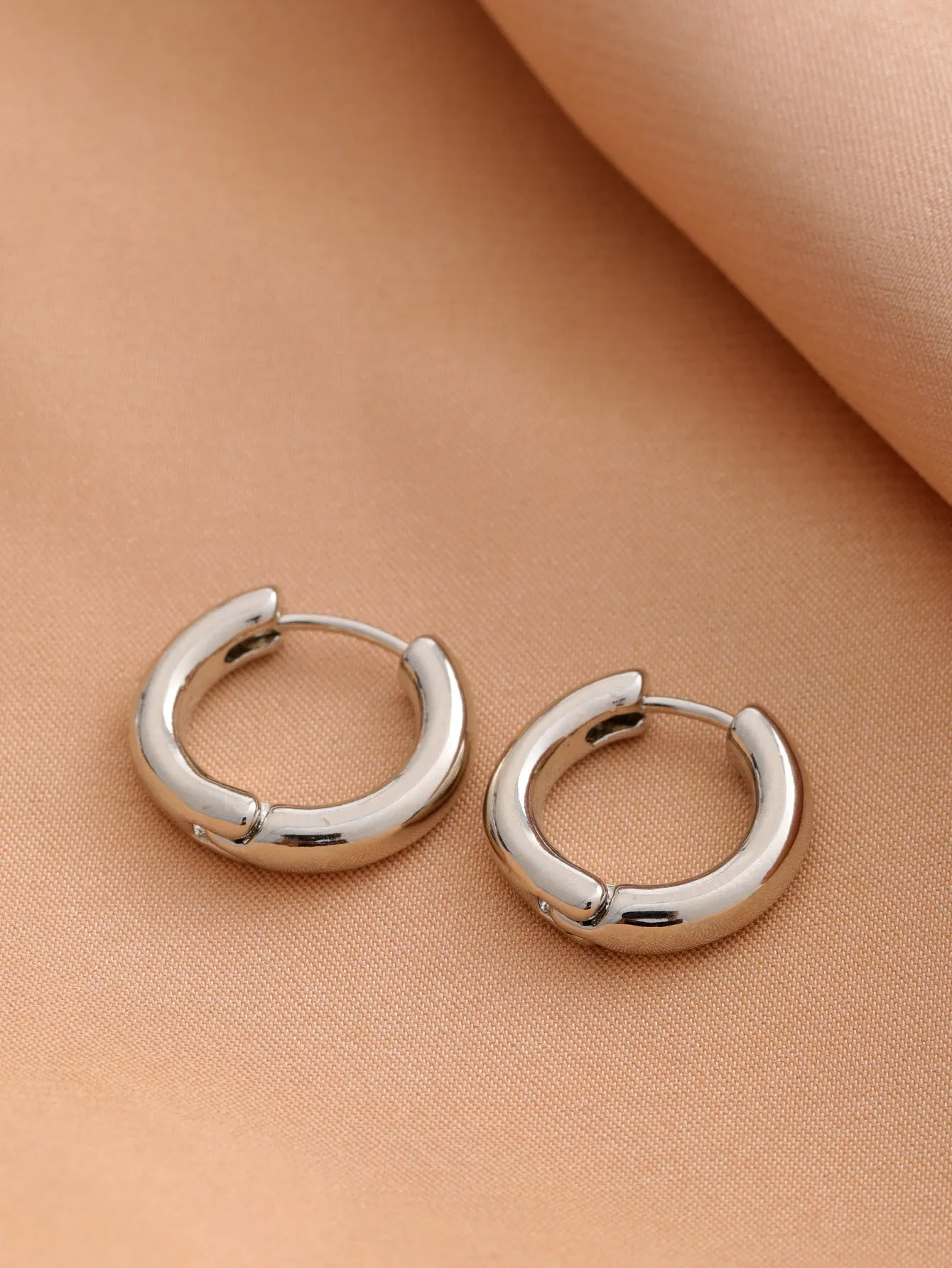Smooth geometric hollow stud earrings in gold and silver colour options on a neutral background