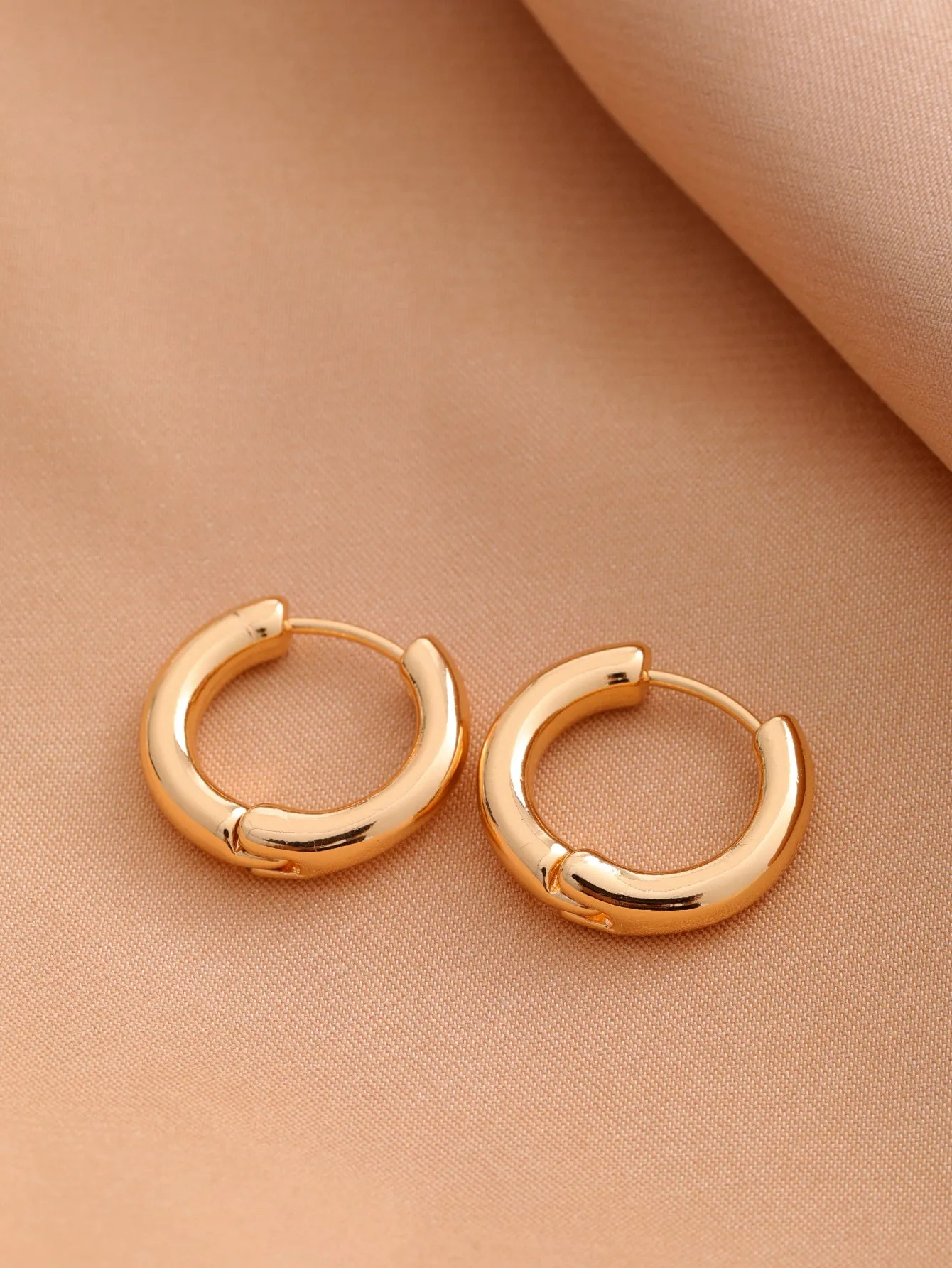 Smooth geometric hollow stud earrings in gold and silver colour options on a neutral background