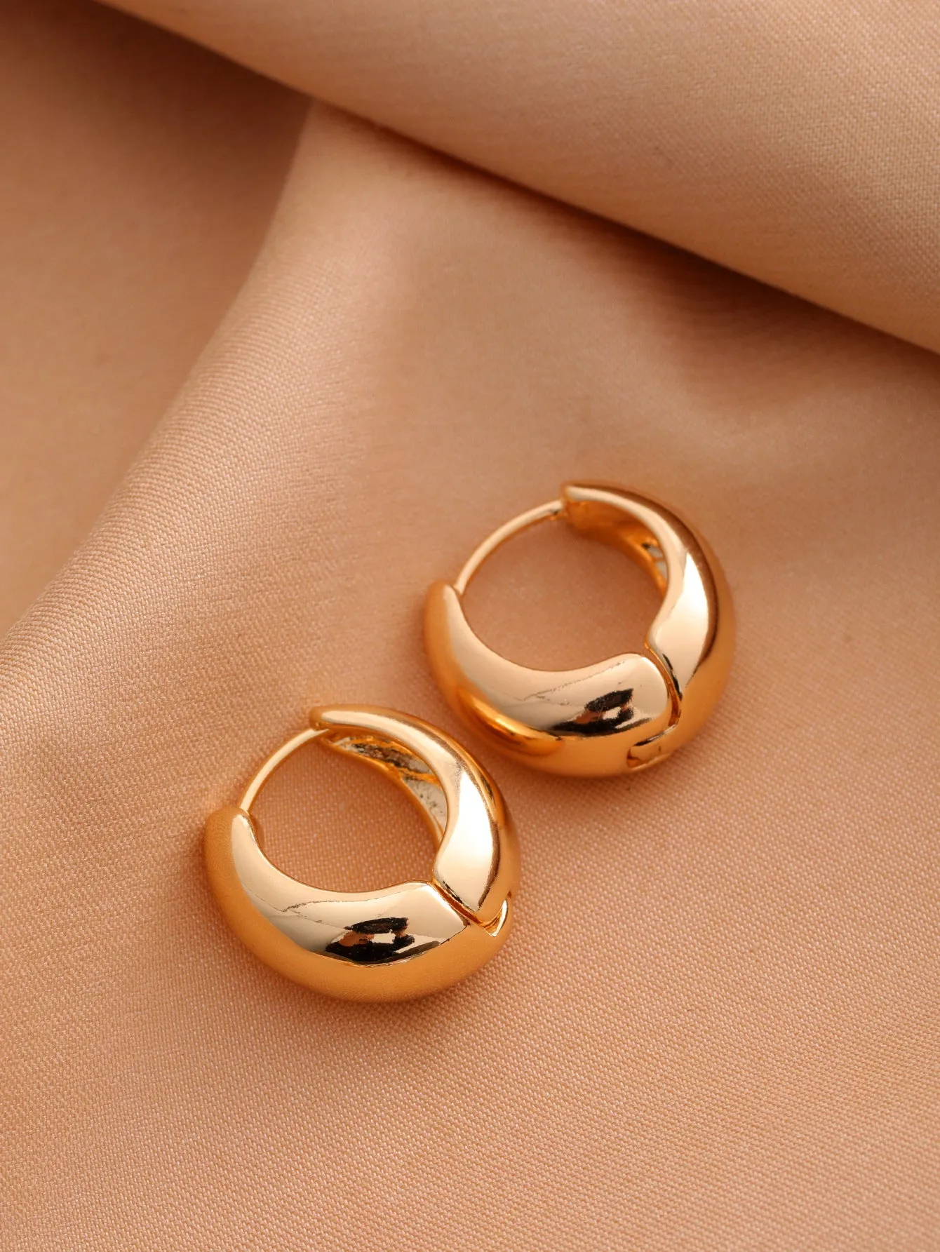 Smooth geometric hollow stud earrings in gold and silver colour options on a neutral background
