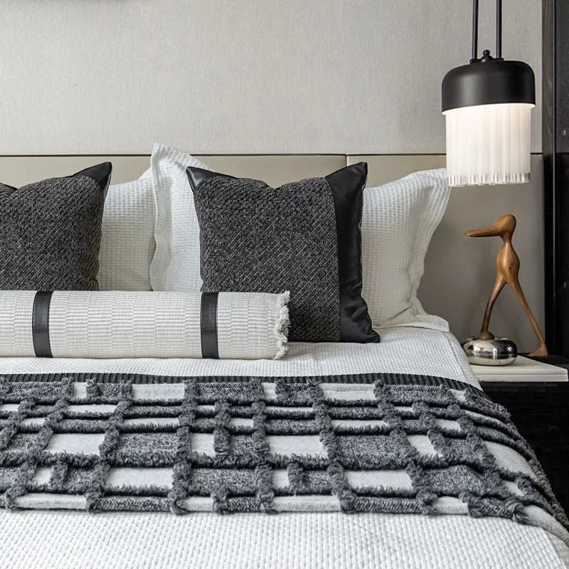 Modern grey and white plaid bed runner blanket set with round leather pillow on a bed.