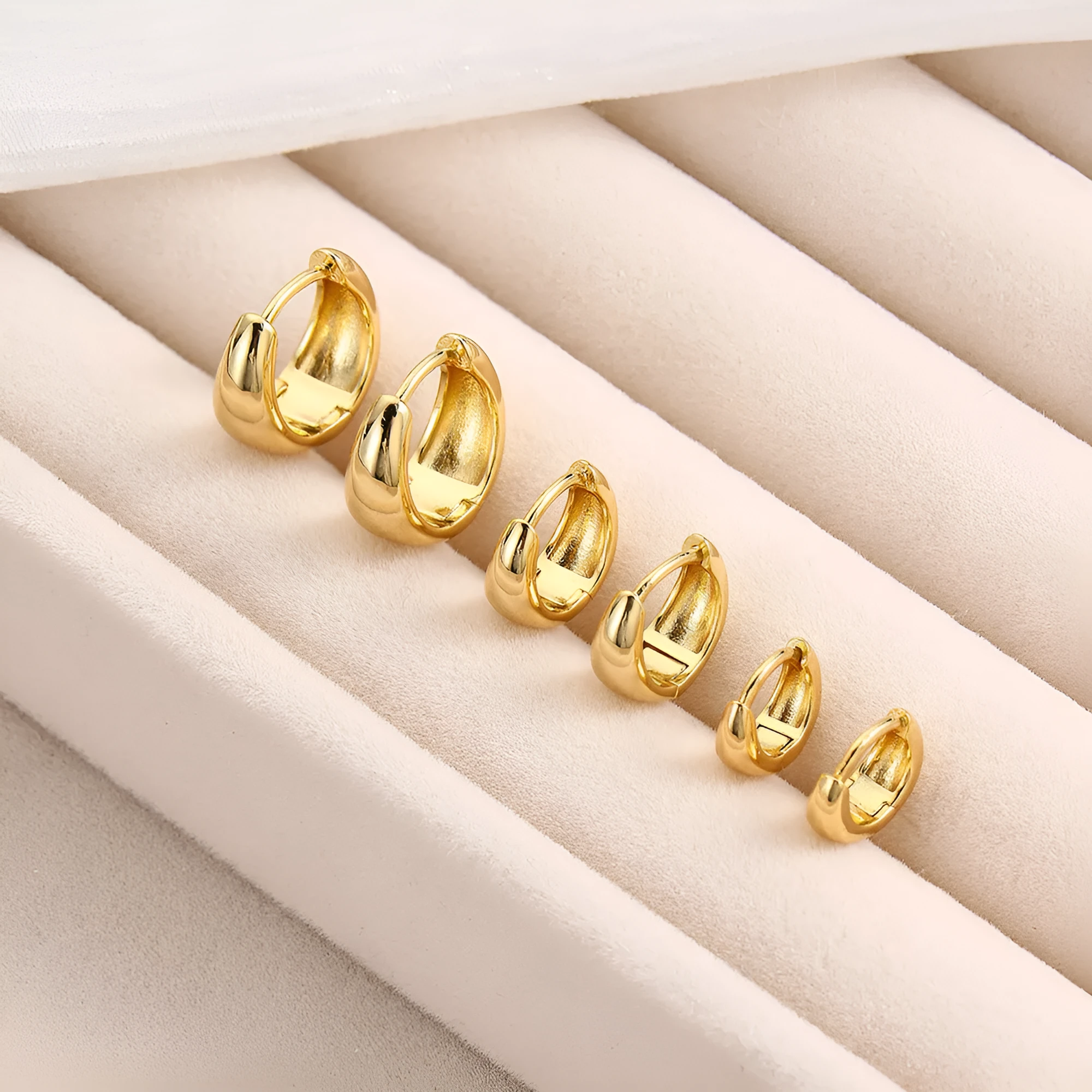 Drop-shaped copper earrings set of three sizes in gold finish on a white background