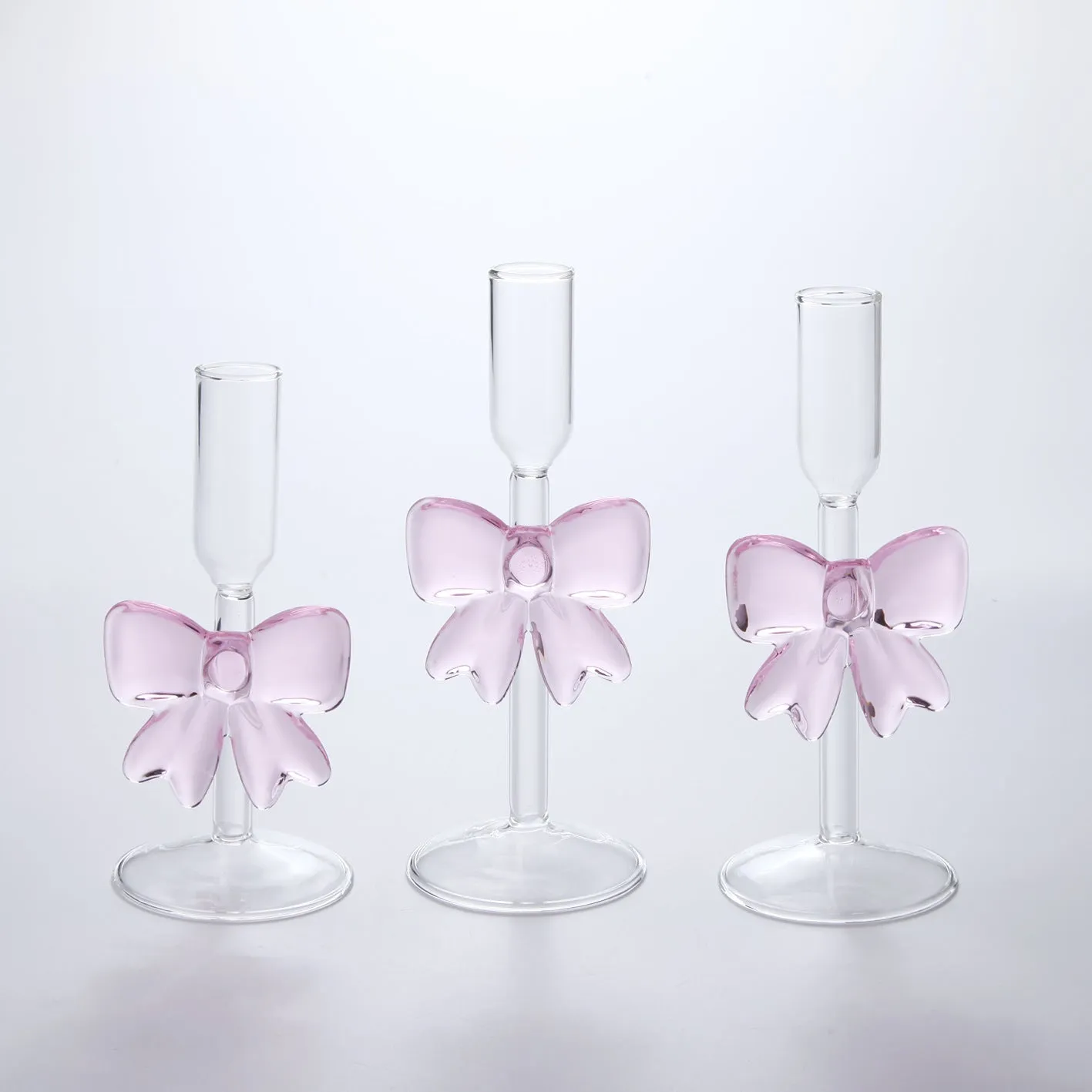 Set of three clear borosilicate glass candlesticks with large bow decorations on a table