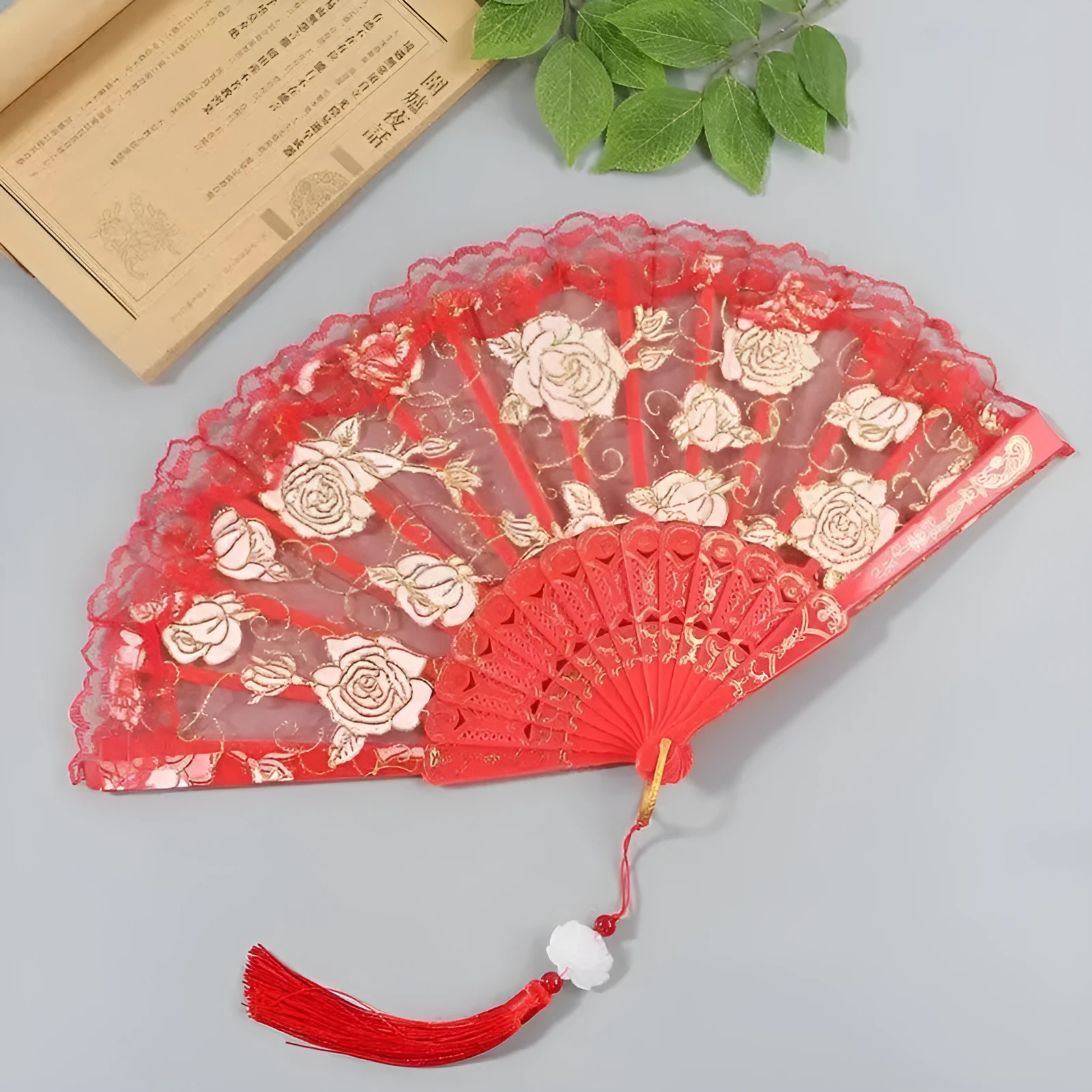 Plastic rose lace folding fan in red with tassel on white background