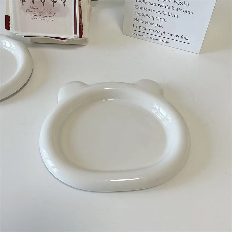 White ceramic plate with cartoon bear doodle design, shown next to round toot design plate, both microwave safe.
