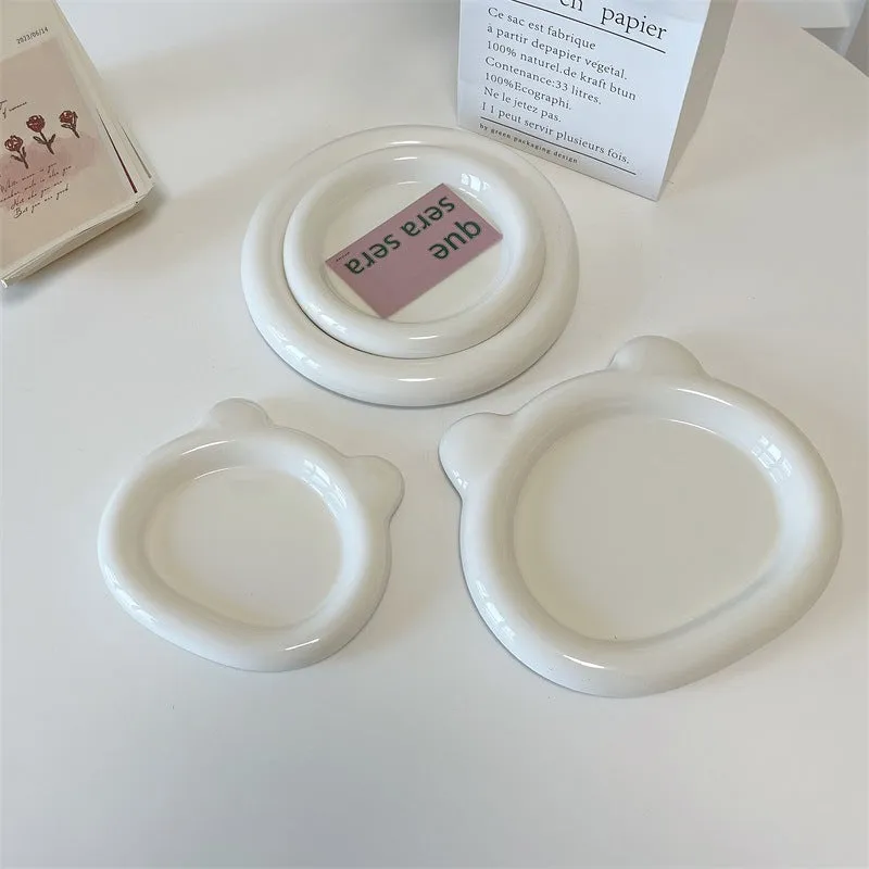 White ceramic plate with cartoon bear doodle design, shown next to round toot design plate, both microwave safe.