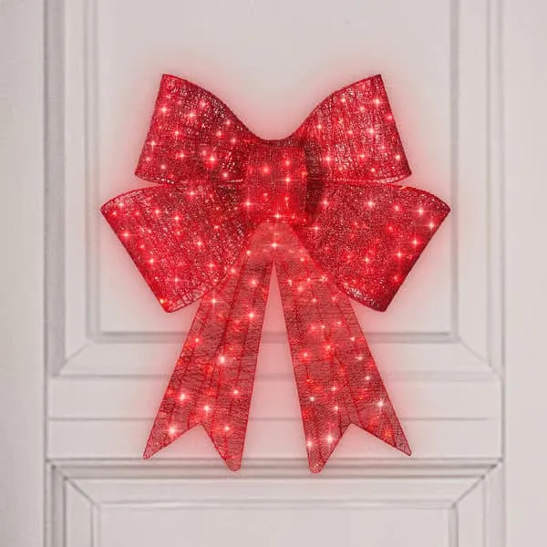Red satin light up Christmas bowknot on a tree branch with warm glow