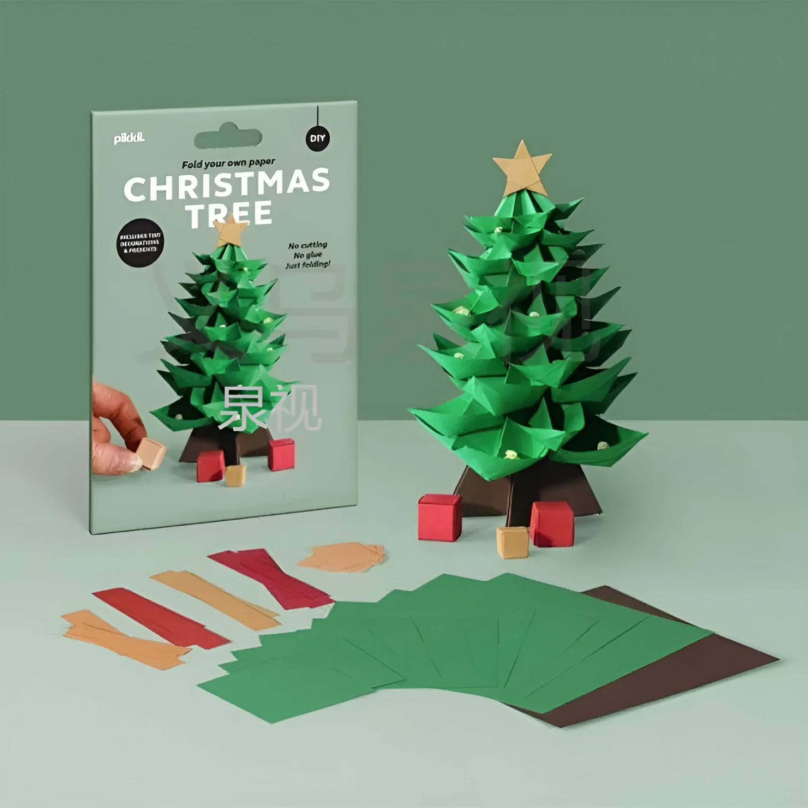 Christmas tree paper folding kit with origami sheets, small scissors, and instruction manual on a desktop